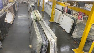 Overhead view of Paramount Quality Stone slab warehouse and showroom, displaying marble, granite, and quartzite slabs neatly arranged in vertical racks beneath yellow overhead cranes.