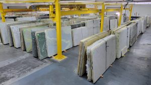 Paramount Quality Stone slab warehouse and showroom with an extensive selection of marble, granite, and quartzite slabs, organized in vertical racks beneath overhead yellow cranes.