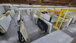 Aerial view of a stone slab warehouse featuring marble, granite, and quartzite slabs stored in vertical racks, with overhead cranes for material handling.