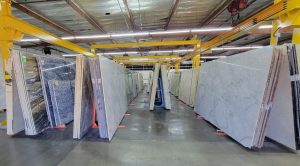 Paramount Quality Stone slab warehouse and showroom featuring marble, granite, and quartzite slabs stored in vertical racks, with overhead cranes for material handling.
